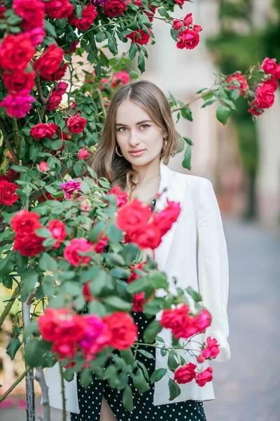 Mladá krásná žena se prochází po evropském městě. Portrét mladé ženy blízko kvetoucích růží. Evropa. — Stock fotografie