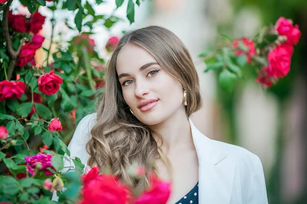 Jovem mulher bonita caminha em uma cidade europeia. Retrato de uma jovem perto de rosas em flor. A Europa . — Fotografia de Stock