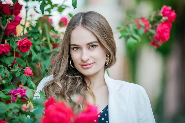 Jovem mulher bonita caminha em uma cidade europeia. Retrato de uma jovem perto de rosas em flor. A Europa . — Fotografia de Stock