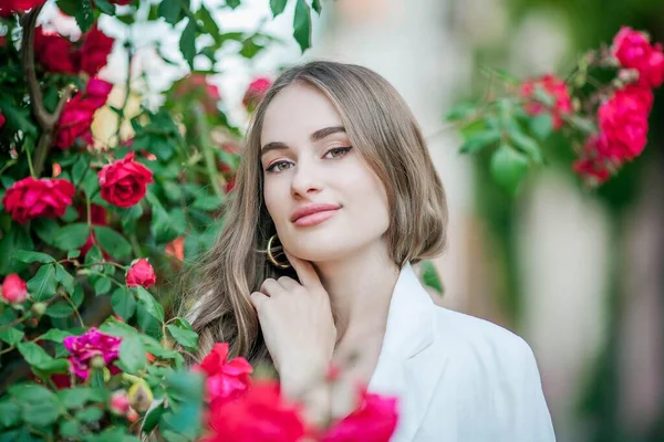 Jovem mulher bonita caminha em uma cidade europeia. Retrato de uma jovem perto de rosas em flor. A Europa . — Fotografia de Stock