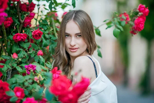 Jovem mulher bonita caminha em uma cidade europeia. Retrato de uma jovem perto de rosas em flor. A Europa . — Fotografia de Stock