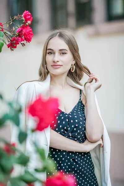 Jovem mulher bonita caminha em uma cidade europeia. Retrato de uma jovem perto de rosas em flor. A Europa . — Fotografia de Stock