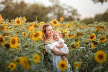Genç ve güzel bir anne küçük kıvırcık bir kız çocuğu tutuyor. Annelik. Kıvırcık anne ve küçük kızı ayçiçeği tarlasında.