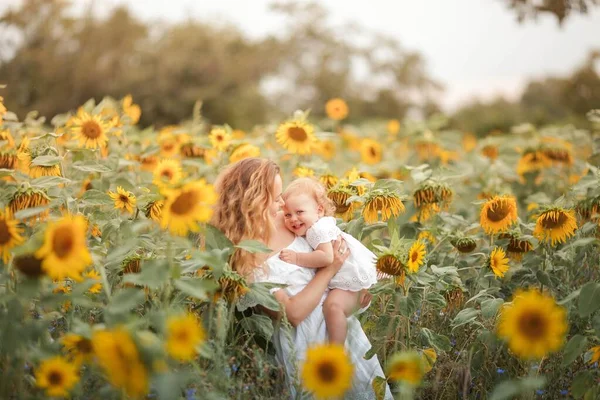 Young beautiful mother holds on hands a little curly daughter. Motherhood. Curly mom and little daughter in a sunflower field.