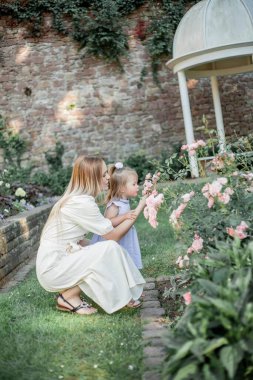 Genç bir anne ve kızı çiçek bahçesinde yürüyorlar. Güller.