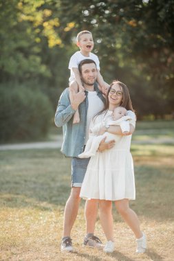 Genç ve güzel bir aile parkta yürüyor. Gün batımında aile portresi. Yaz pikniği. Bahar.