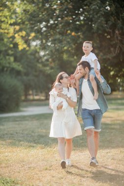 Genç ve güzel bir aile parkta yürüyor. Gün batımında aile portresi. Yaz pikniği. Bahar.