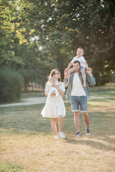 Young beautiful family walks in the park. Family portrait in the sunset light. Summer picnic. Spring.