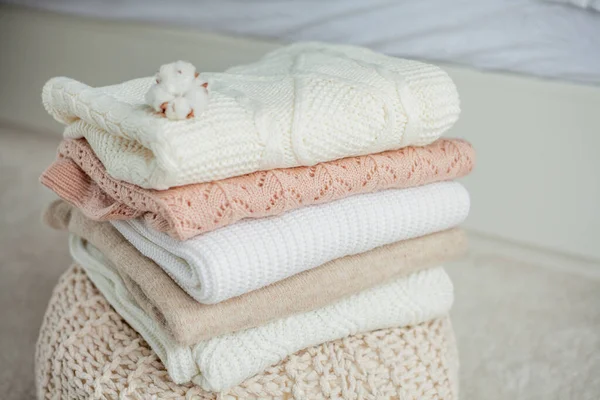 A stack of knitted sweaters, cotton. Women's sweaters lie on the ottoman. Cozy autumn clothes. Fall.