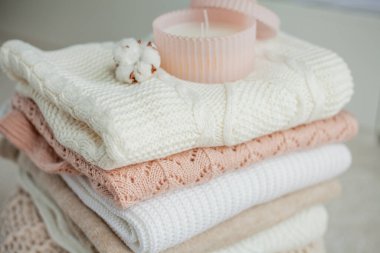 Bir yığın örgü kazak, pamuk, cam kavanozda bir mum. Kadın bluzları kanepenin üzerinde. Sıcak sonbahar kıyafetleri. Düş.