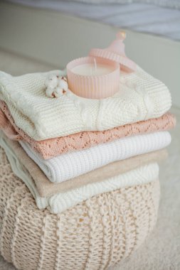 Bir yığın örgü kazak, pamuk, cam kavanozda bir mum. Kadın bluzları kanepenin üzerinde. Sıcak sonbahar giysileri.