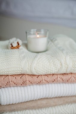 Bir yığın örgü kazak, pamuk, mum. Kadın bluzları kanepenin üzerinde. Sıcak sonbahar giysileri.