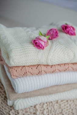 Bir yığın örgü süveter, güller. Kadın kazakları kanepenin üzerinde yatıyor. Sıcak sonbahar giysileri.