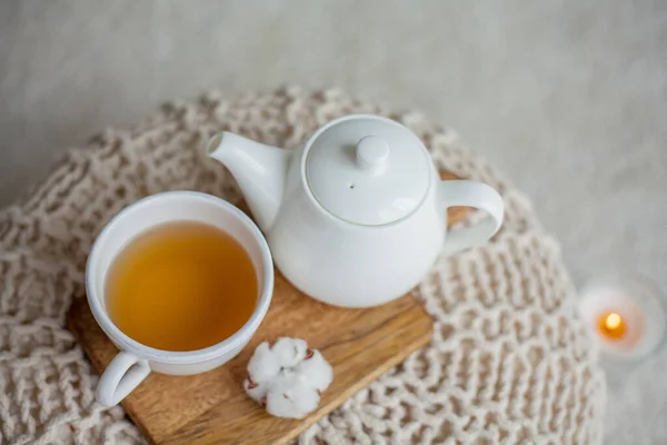 A stack of knitted sweaters, a mug of hot tea, a teapot, a wooden stand on an ottoman. Cozy autumn. Winter breakfast. Roses. Candle. — Stock Photo, Image