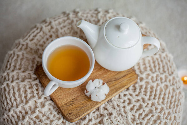 A stack of knitted sweaters, a mug of hot tea, a teapot, a wooden stand on an ottoman. Cozy autumn. Winter breakfast. Roses. Candle.