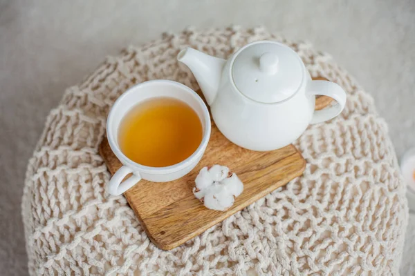 Une tasse de thé chaud, une théière, un support en bois sur un pouf. Confortable automne. Petit déjeuner d'hiver. Coton. — Photo