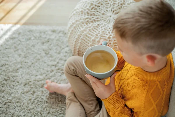 一个穿着橙色毛衣的可爱小男孩正在喝茶 一个坐在家里的男孩舒适的肖像 — 图库照片