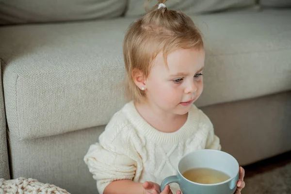 オレンジのセーターを着た可愛い女の子がお茶を飲んでいます 家に座っている女の子の居心地の良い肖像画 — ストック写真