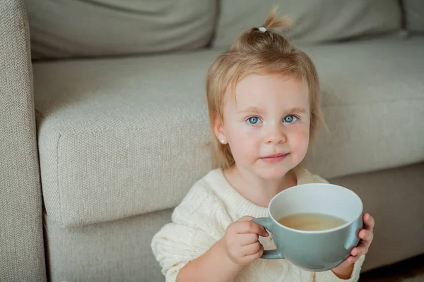 オレンジのセーターを着た可愛い女の子がお茶を飲んでいます 家に座っている女の子の居心地の良い肖像画 — ストック写真
