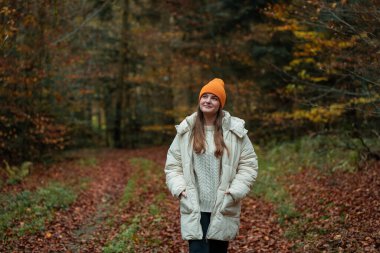 Sonbahar ormanında şapkalı ve kalın elbiseli genç bir kızın portresi. Doğada meditasyon.