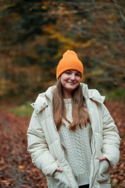 Sonbahar ormanında şapkalı ve kalın elbiseli genç bir kızın portresi. Doğada meditasyon.