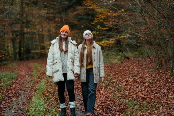 Genç kız kardeşler sıcak kıyafetler içinde, sonbahar ormanlarında şapkalar takıyorlar. Doğada meditasyon ve rahatlama.