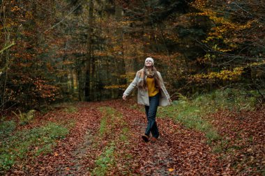 Sonbahar ormanında yürürken şapkalı ve kalın elbiseli mutlu bir genç kızın portresi. Doğada meditasyon.