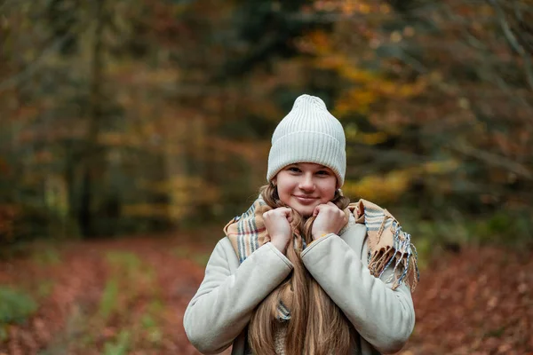 Sonbahar ormanında yürürken şapkalı ve kalın elbiseli mutlu bir genç kızın portresi. Doğada meditasyon.