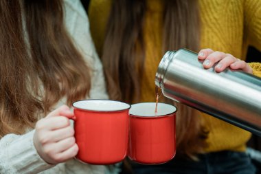 Genç kız kardeşler sonbahar ormanlarında kırmızı bir arabanın bagajında büyük bir termostan sıcak çay içiyorlar. Piknik.