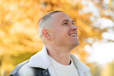 Sarı bir sonbahar parkının arka planında, rahat ceketli gülümseyen bir adamın portresi..