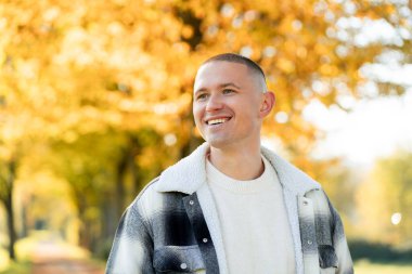 Sarı bir sonbahar parkının arka planında, rahat ceketli gülümseyen bir adamın portresi..