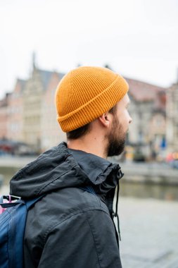 Elinde akıllı bir telefonla sonbahar kıyafetleri içinde sakallı bir adamın portresi. Eski bir Avrupa şehrinde sırt çantalı bir turist.