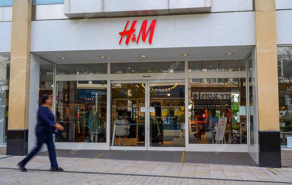 Bromley (Greater London), Kent, UK. H&M store in Bromley High Street with a blurred pedestrian walking past. H&M shop with reflections in the windows.