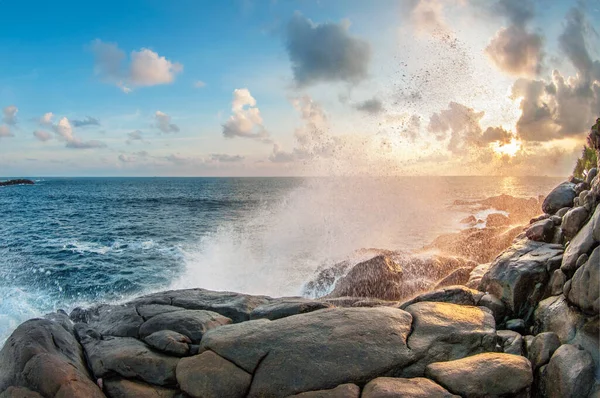 Gün batımında dalgalar kayaların üzerinde kırılır. Güneşin ışınları bulutları delip ıslak taşları aydınlatıyor. Sri lanka.