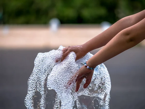 Girl\'s hand playing with a stream of water from a fountain