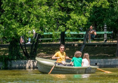 Bükreş / Romanya - 05.30,2020: Annem ve çocukları Bükreş 'teki Cismigiu parkında bir botta. Kürek çeken kadın.