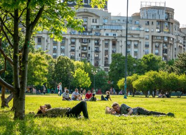 Bükreş / Romanya - 05.30.2020: Bükreş 'in merkezinde çimlerin üzerinde uzanan insanlar, Coronavirus' un tecridinin kaldırılmasının ardından güzel bir günün keyfini çıkarıyorlar.