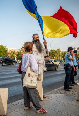 Bükreş / Romanya - 09.19.2020: Yüz maskesi takmaya karşı Üniversite meydanında düzenlenen protestoda büyük bir Romen bayrağı sallayan adam.