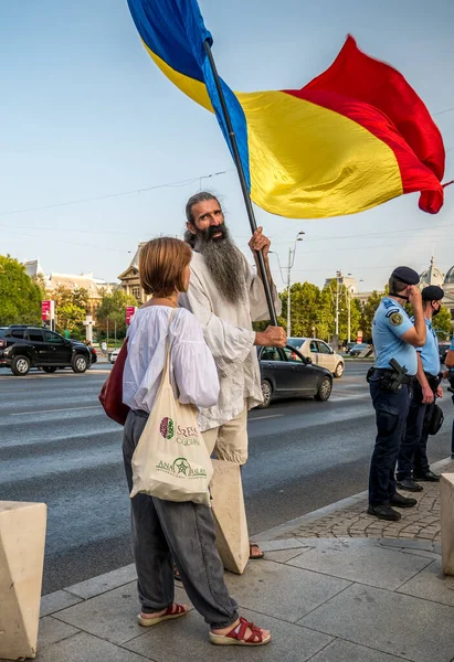 Bükreş / Romanya - 09.19.2020: Yüz maskesi takmaya karşı Üniversite meydanında düzenlenen protestoda büyük bir Romen bayrağı sallayan adam.