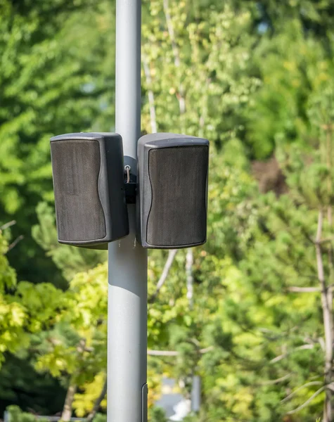 Black speakers suspended from a metal pole with blue sky as a background. Outdoor speakers for music .