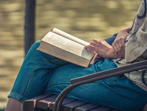 Parktaki bankta oturan ve kitap okuyan bir kadın.