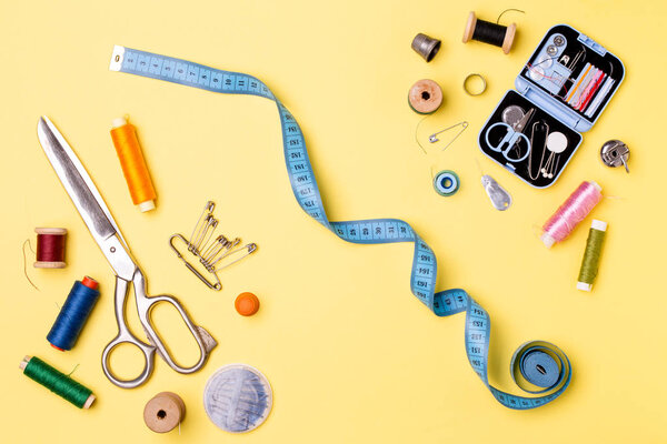 Composition with threads and sewing accessories - scissors, centimeter, pins on yellow background.