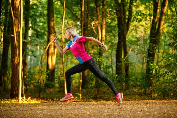 Foto från sidan av sport kvinna löper genom parken bland träden på sommaren. — Stockfoto