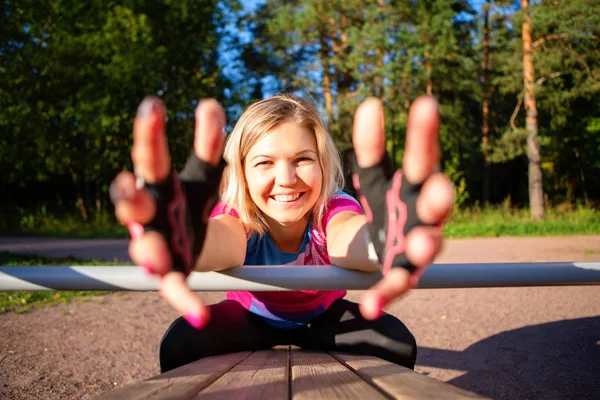 Sportlerin, die die Hände nach vorne zieht, trainiert im Sommer an Holzbank im Park. — Stockfoto