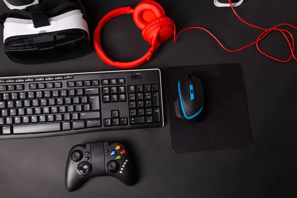 Top view a gaming gear, mouse, keyboard, joystick, headset, VR Headset on black table background.