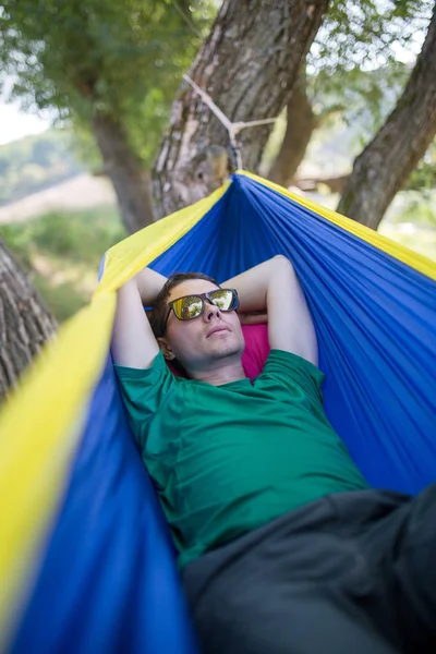 Foto de hombre en gafas de sol tumbado en la hamaca en el bosque —  Fotos de Stock