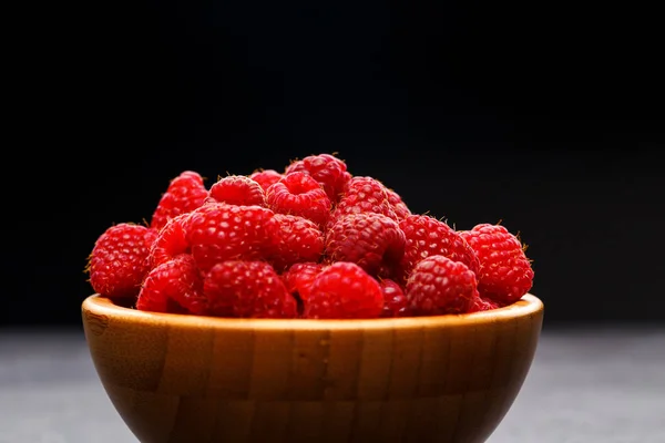 Photo of raspberries in wooden cup on black background — Stock Photo, Image