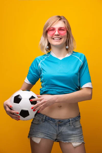 Foto de rubia en gafas de color rosa con pelota de fútbol sobre fondo naranja —  Fotos de Stock