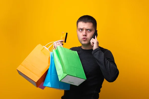 Foto de hombre comprador con bolsas de papel, tarjeta bancaria y teléfono en la mano — Foto de Stock