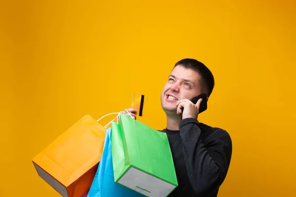 Foto de hombre comprador con bolsas de papel, tarjeta bancaria y teléfono en la mano — Foto de Stock